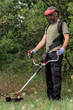 © zphoto83 - Man using a brush cutter to maintain grass in a wooded area during a sunny afternoon