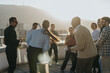 © qunica.com - A diverse group of business people celebrate success on a high rooftop at sunset, enjoying music and dancing while sharing joyful moments together against a beautiful cityscape backdrop.
