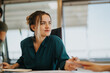 © qunica.com - A confident businesswoman in a teal blouse sits attentively during a meeting. The setting conveys a professional and collaborative atmosphere, emphasizing focus and engagement.