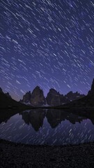 Wall Mural - time-lapse video concept of star trails over mountains, reflected in a lake. captured from a low ang