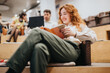 © qunica.com - A happy woman sitting comfortably while reading a book in a contemporary office space, with co-workers collaborating in the background, creating a relaxed and focused atmosphere.