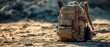 © Liliant - Military-style backpack on a sandy desert ground under sunlight