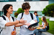 © djile - Two male college students discussing notes from a textbook while walking outdoors on a university campus