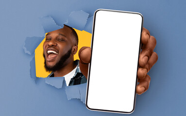 Poster - Recommendation. Excited black guy holding big smartphone with white blank screen in hand, showing close to camera through torn blue paper hole. Gadget with empty free space for mock up, banner