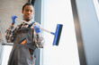 © Serhii - African American Professional cleaning service worker washing windows with squeegee