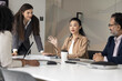 © fizkes - Group of diverse professionals engaged in discussion at conference table in office, listening young female Asian leader explaining or presenting idea. Formal business meeting event or brainstorming