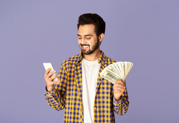 Poster - Millennial Indian guy with cash making money online on mobile phone, lilac background
