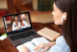 © Prostock-studio - Online education, e-learning concept. Young woman with earbuds having video conference with male teacher, sitting at desk and using laptop, taking notes, discussing studying material, home interior