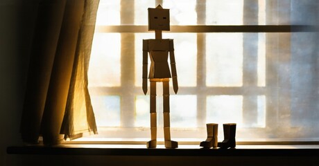 Aufkleber - Paper figure stands near window. Light creates dramatic shadows, highlighting simple form, boots nearby. Quiet, contemplative scene.