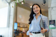 © Phimwilai - Young asian businesswoman smiling and holding laptop in office hallway