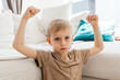 © Elena - Confident Young Boy Flexing Arms on Sofa