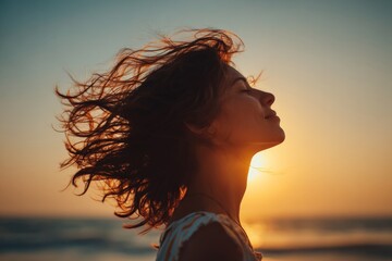 Poster - Woman enjoying sunset at the beach with wind blowing through her hair in a serene atmosphere