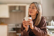 © Iryna - Woman enjoying a quiet moment holding a cup of coffee in a cozy kitchen during morning hours