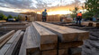 © Jack - Freshly cut lumber is stacked prominently in the foreground, while construction workers engage at a nearby building site. This scene captures the progress of new homes being built