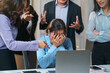 © Crystal - Colleagues pointing at businesswoman covering face with hands while sitting at desk in office meeting, concept of business failure and workplace bullying