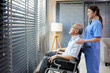 © offsuperphoto - nurse or caregiver standing beside elderly man sitting on wheelchair and looking outside at home