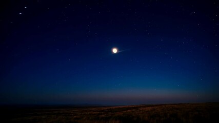 Wall Mural - Full moon rising over golden field at night under a starry deep blue sky with wispy clouds creating an eye effect