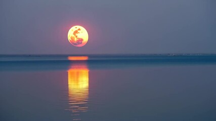 Wall Mural - Full moon rising over serene water with reflection and beautiful sky colors during evening twilight hours