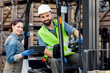 © Prostock-studio - Warehouse workers, industry management with modern technology. Smiling millennial woman with tablet speaks with bearded man in helmet in forklift truck check order, on many wooden boxes background