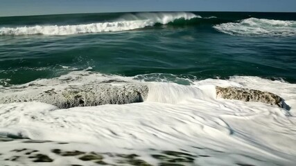 Poster - Turbulent ocean water crashing over rocks, creating white foam and sea spray in a dynamic, abstract seascape visual background element.