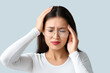 © Pixel-Shot - Young Asian woman suffering from headache on grey background. Brain Injury Awareness Month