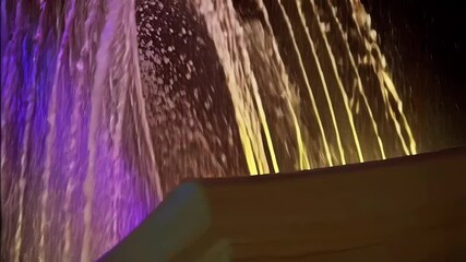 Poster - Illuminated water fountain cascade featuring vibrant purple and yellow hues, creating a dynamic display of flowing water streams