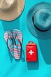 © Milana - Two summer straw hats, striped flip-flops, and a red first aid kit arranged on a bright turquoise surface evoking a sunny beach or vacation vibe
