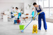 © Pixel-Shot - Male janitor mopping floor with his team in office