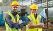 © BESTIMAGE - Two happy factory workers wearing hard hats and safety vests standing with arms crossed.
