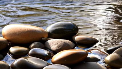 Poster - Smooth river rocks and pebbles submerged in flowing water, creating ripple patterns and serene natural scenery