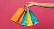 © Muhammad - A woman's hand gripping multiple vibrant shopping bags against a neutral gray backdrop.