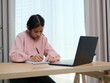 © Wichayada - A girl is sitting at a desk with a laptop and a notebook