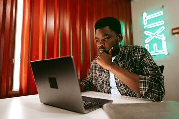 Poster - Focused man working on a laptop in a modern workspace with creative lighting