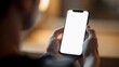 © Ahmad - A person holds a black smartphone with a blank white screen, viewed in a softly lit indoor environment.