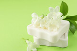 Bars of soap and jasmine flowers on light green background, closeup. Space for text