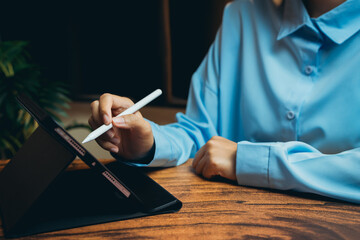 Poster - Person Using Stylus on Digital Tablet While Sitting at Wooden Table in Modern Office Environment