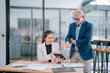 © Tj - Senior manager coaching young businesswoman using tablet and analyzing financial charts while working together on new project in modern office