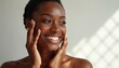 © Maryna - Beautiful black woman with radiant skin smiles while touching face on white background. Beauty and spa advertisement, poster, copy space. Concept of skincare, wellness, rejuvenation.