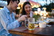 © saltdium - A beer glass sits in focus as two friends laugh and enjoy street food together, capturing a lively and relaxed evening at an outdoor night market