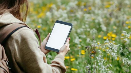 Poster - A woman looks at her cell phone while standing outdoors with a backpack, possibly on a hike or adventure