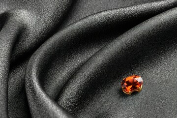 Poster - Shiny orange gemstone placed elegantly on soft black fabric highlighting its brilliance and design