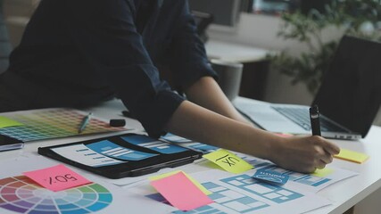 UX/UI designer working on wireframes for a website and mobile app prototype, surrounded by sketches of user-flow and design tools, in concept of website and mobile application design concept.