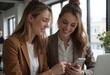 © starush - Two women collaborating in a modern office, sharing ideas on a smartphone
