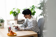 © Studio Marmellata - A woman is working on her laptop at a desk in a bright, plant-filled room. She's smiling, likely enjoying her work or connecting with someone online.