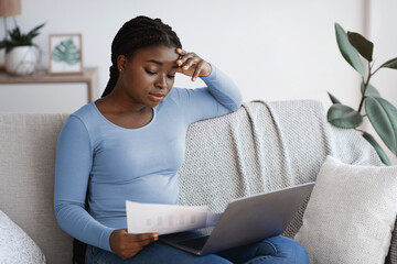 Aufkleber - Remote Business. Pensive african woman checking papers and working with laptop at home, thoughtful black female freelancer busy with financial reports and documentation, sitting on sofa in living room
