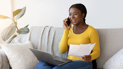 Poster - Work From Home. Smiling Black Freelancer Lady Talking On Cellphone While Working With Papers And Laptop On Couch In Living Room, African Lady Enjoying Remote Job And Mobile Communication, Copy Space