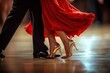 © Donna - Close-up of a dancing couple's legs with a woman wearing a flowing red dress and glittery gold high heels and a man in black dress shoes, capturing grace and elegance