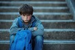 © kong - sad young boy with blue backpack sits on outdoor stone steps with arms crossed looking upset and serious