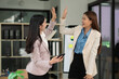 © panomporn - Two excited Asian businesswomen raising their arms and delighted at a successful company event in an office environment.