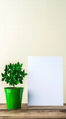 Poster - Green plant placed next to a blank paper sheet on a simple surface creating a minimalist workspace